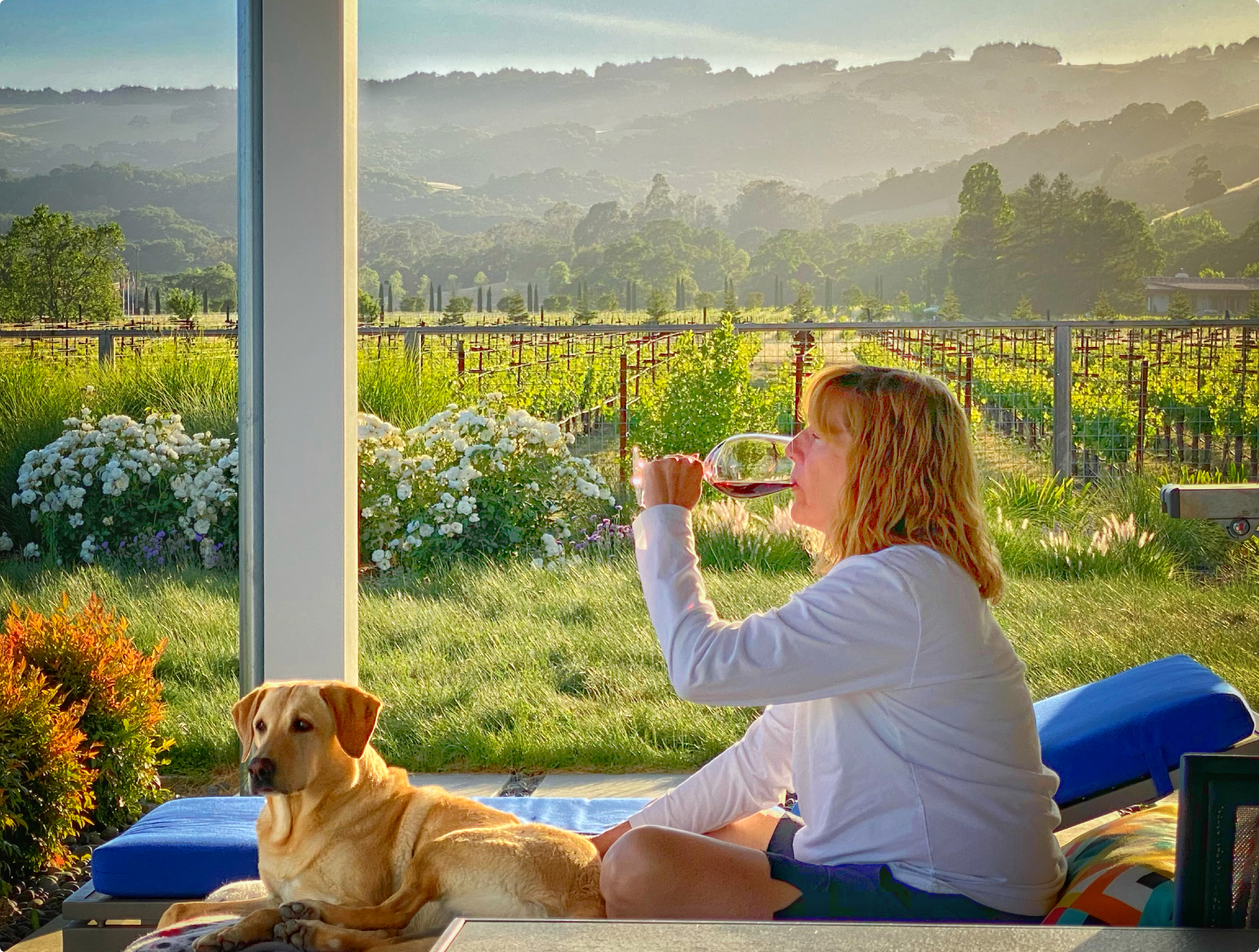 Woman sitting on a couch with her dog, enjoying a glass of wine